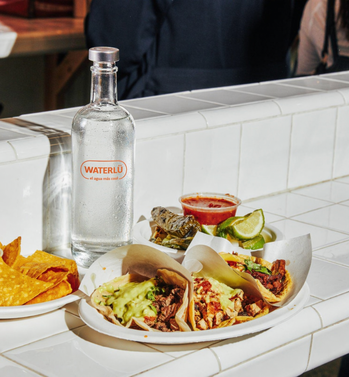 Botella WATERLÜ con tacos en restaurante